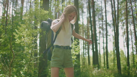 A-young-female-blonde-tourist-walks-through-the-woods-in-slow-motion-with-a-backpack-passing-through-a-log-during-an-adventure